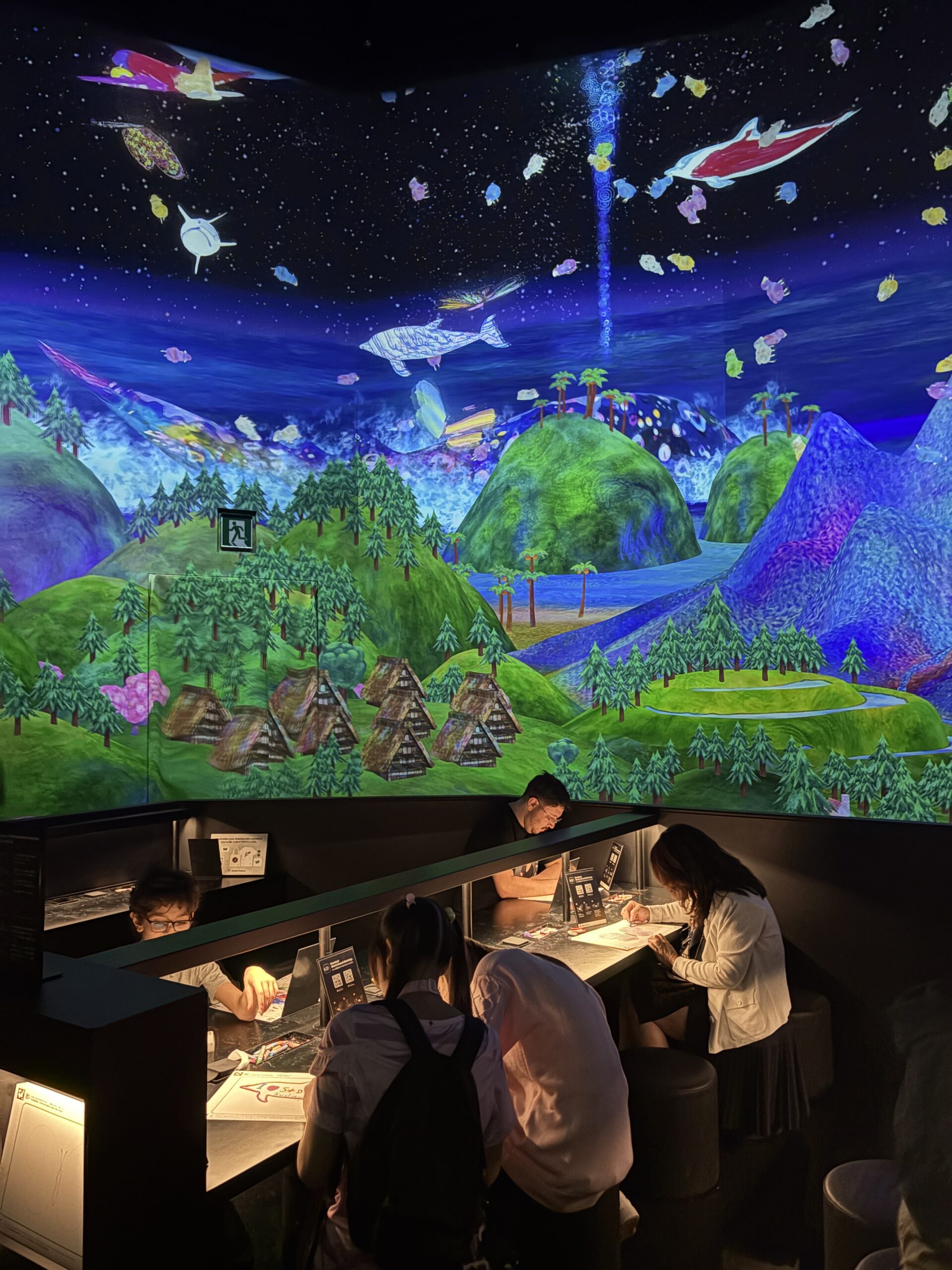 Visitors drawing creatures beneath a colorful interactive projection at teamLab Planets Tokyo